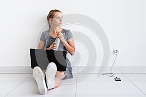 Young woman working with laptop from home, sitting on the floor and drinking water