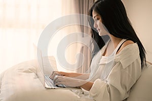 Young woman working on a laptop sitting on bed at home