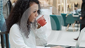 young woman is working on a laptop and taking notes in a notebook.