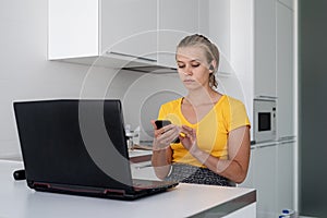 Young woman working with laptop and texting on the mobile phone from home