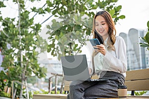 Young woman working laptop and using mobile smartphone outdoor building exterior