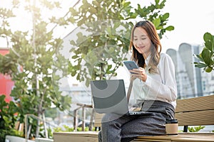 Young woman working laptop and using mobile smartphone outdoor building exterior