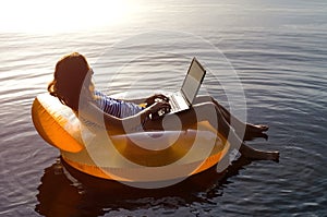 Young woman working on a laptop in the water on an inflatable ri