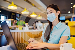 Young woman working on laptop, wearing protective face mask.Online training education and freelance work.Studying remotely.