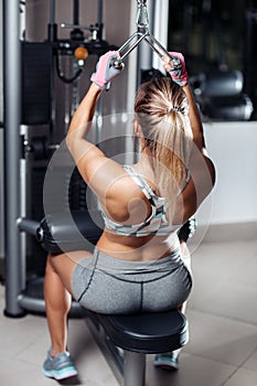 Young woman working at the lat pulldown machine in the gym.