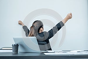 A young woman working in an office with her back facing down, relaxed, arms raised due to her head on an office chair