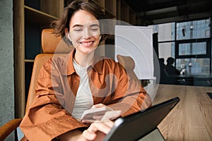 Young woman working in office, sitting with digital tablet, waiting for a meeting in conference room