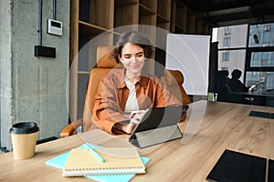 Young woman working in office, sitting with digital tablet, waiting for a meeting in conference room