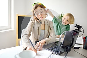 Young woman working online using laptop at home. Home office and parenthood at same time. Exhausted parent with hyperactive child