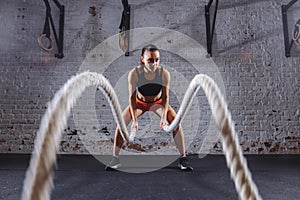 Young woman working out with battle ropes in cross fit gym