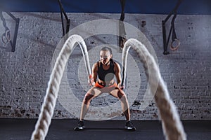 Young woman working out with battle ropes in cross fit gym