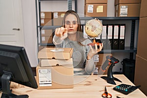 Young woman working at small business ecommerce holding world ball pointing with finger to the camera and to you, confident