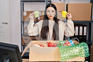 Young woman working at small business ecommerce selling cups looking at the camera blowing a kiss being lovely and sexy