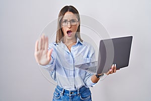 Young woman working using computer laptop doing stop gesture with hands palms, angry and frustration expression