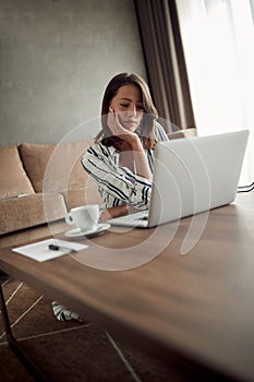 Young woman works for a computer from a home with a laptop as a freelancer