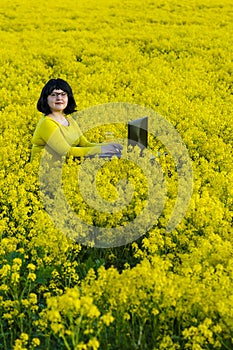 A young woman works in a field among yellow flowers at a table with a laptop.