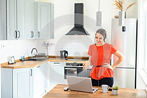 Young woman works from home using headset, laptop