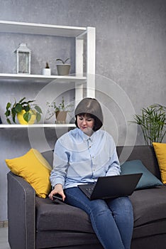 Young woman works at a laptop while sitting at home on the couch. Freelancer at home office. Work on maternity leave