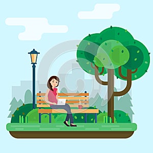 Young woman works in park with computer on bench under tree.