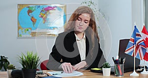 A young woman works in a travel agency, on laptop computer, sitting at a table on the background of a world map