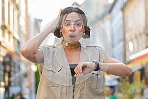 Young woman worrying to be punctual, with anxiety checking time on watch, running late to work