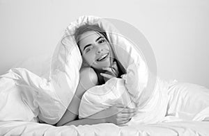Young woman wrapped in soft blanket sitting on bed. Smiling girl sitting in bed and smiling at home.
