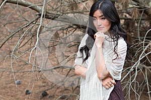 Young woman wrapped in a white scarf stays in forest