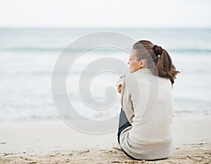 Young woman wrapping in sweater while sitting on lonely beach