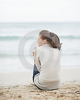 Young woman wrapping in sweater while sitting on lonely beach