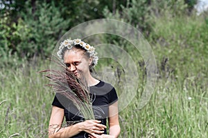 Young woman with a wreath of daisies on her head in the sun on a field of grass
