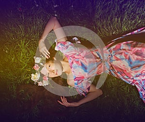 young woman in wreath from folwers on a green grass