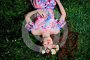 young woman in wreath from folwers on a green grass