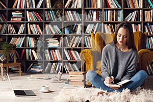 Young woman writer in library at home creative occupation sitting writing notes