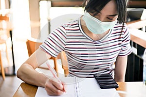 Young woman writes in a notebook ,High school student taking notes while wearing face mask due to coronavirus emergency