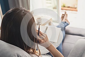 Young woman writing diary at cozy home on sofa