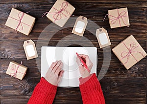 Young woman writing letter to Sante on dark wooden table with presents