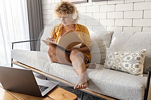 Young Woman Writing in Notebook at Home with Laptop