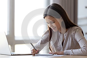 Young woman writing notes in notebook making list planning tasks