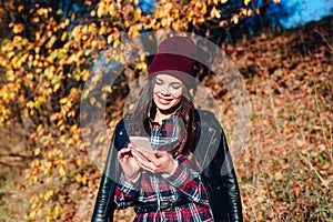 Young woman writting sms on mobile phone in autumn park.