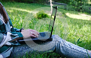 Young woman& x27;s legs on the green grass with open laptop. Girl& x27;s hands on keyboard. Distance learning concept