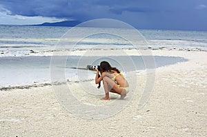 Young woman in yellow bikini takes photographs on the beach