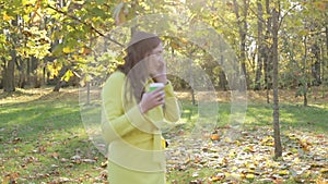 Young woman in a yellow coat walking in the park and talking on the phone.