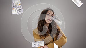 Young woman in yellow costume is posing on white background among flying cash in air in slowmo