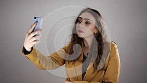 Young woman in yellow costume is standing on white background and making selfie in slowmo