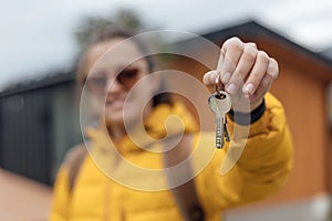 A young woman in a yellow down jacket holds the keys to a vacation home in a mountain area