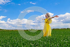 Young woman in yellow dress outdoors in green field. The concept of love of life and openness to the world