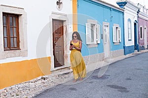 Young woman in yellow dress walking with smart phone on the old streets in the city. Portugal. Travel concept