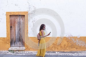 Young woman in yellow dress walking with smart phone on the old streets in the city. Portugal. Travel concept