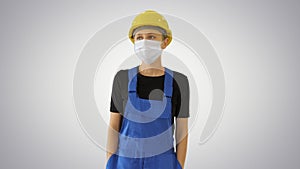 Young woman in yellow hardhat and in medical mask walking on gradient background.