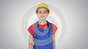 Young woman in yellow hardhat walking on gradient background.